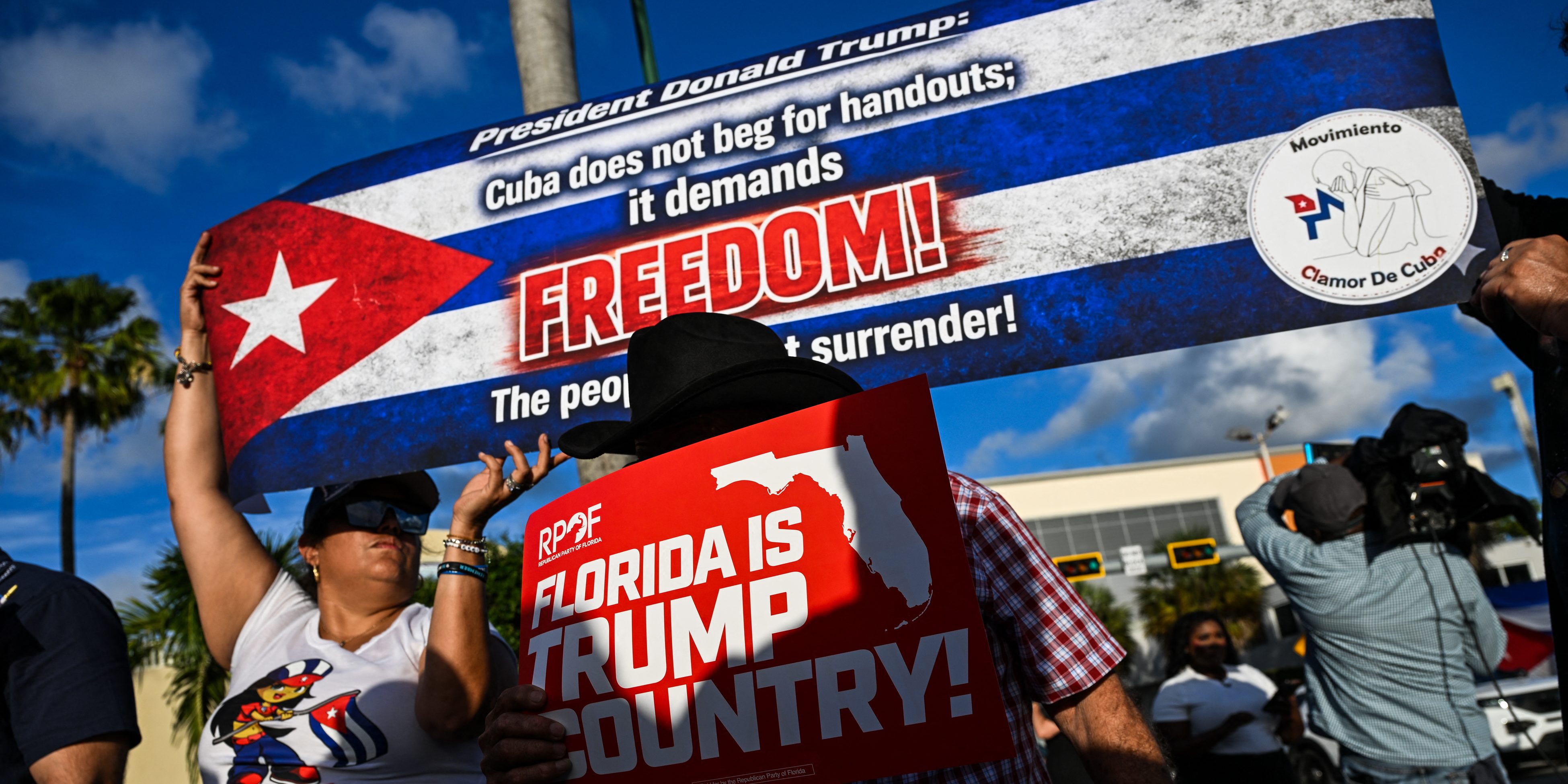 People hold signs outside Versailles Restaurant in support of charges announced by federal prosecutors against the former Cuban president in Miami, Florida, on May 20, 2026.