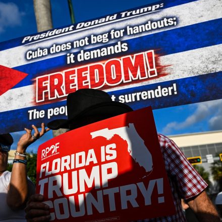 People hold signs outside Versailles Restaurant in support of charges announced by federal prosecutors against the former Cuban president in Miami, Florida, on May 20, 2026.