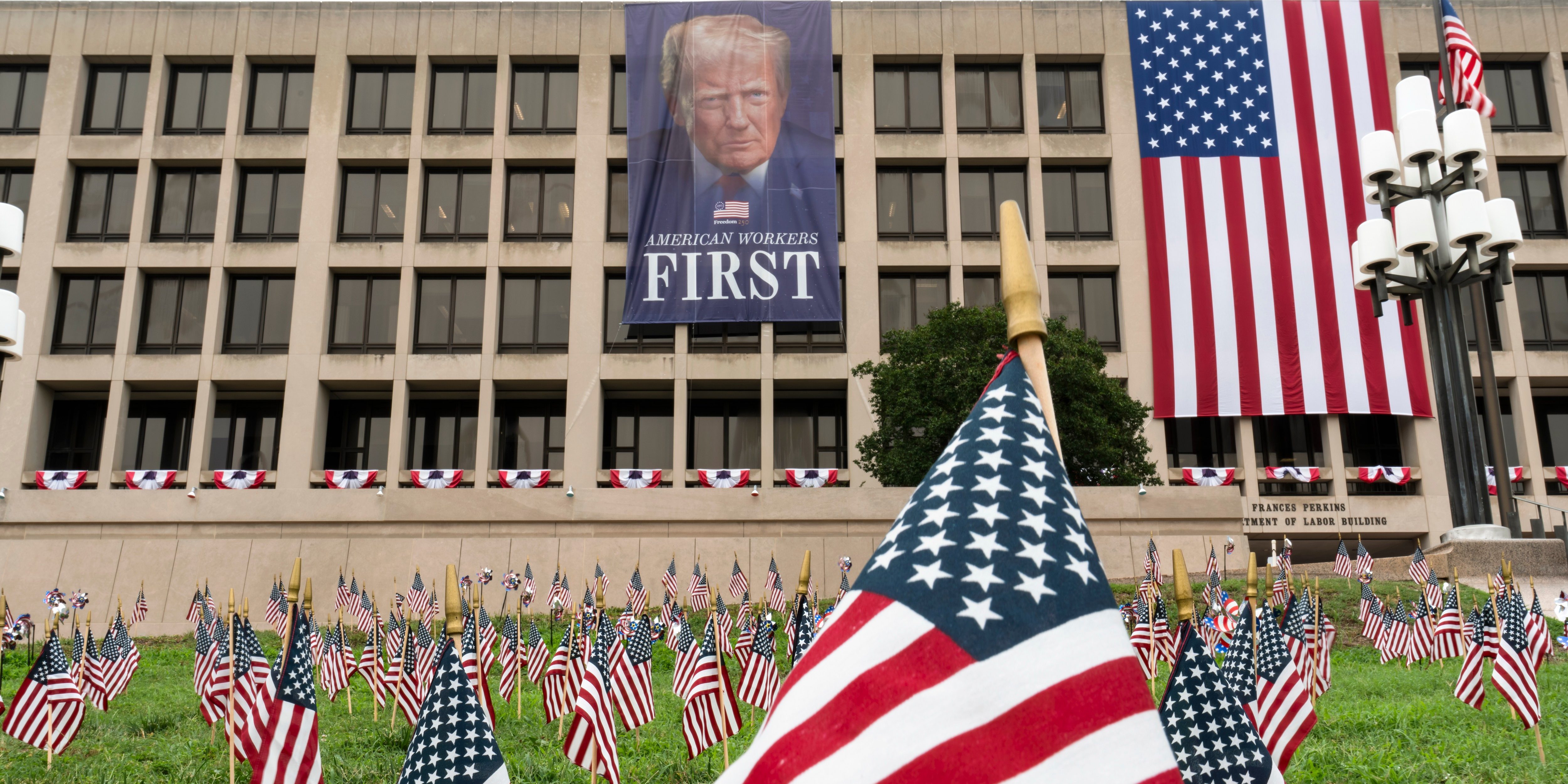 A large portrait of President Donald Trump looms over a field of American flags at the Department of Labor in Washington, Tuesday, July 7, 2026.