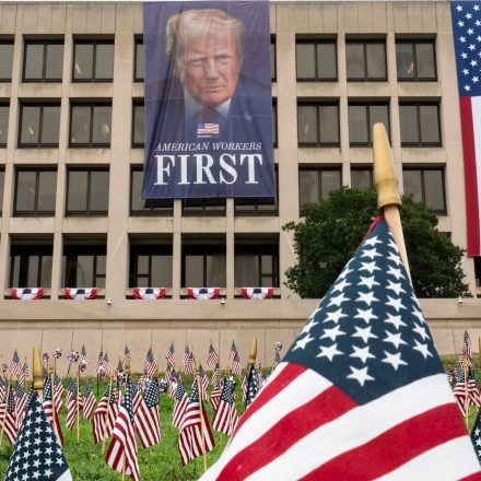 A large portrait of President Donald Trump looms over a field of American flags at the Department of Labor in Washington, Tuesday, July 7, 2026.