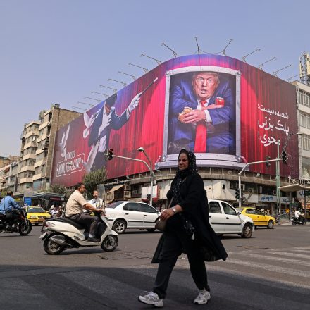 A pedestrian walks past a billboard depicting US President Donald Trump inside a catering container, installed on a building along a street in downtown of Tehran on August 31, 2026. Iran attacked US military targets in the Middle East on August 31 in retaliation for American strikes on an island in the Strait of Hormuz, the first exchange of fire for a month in a war that has engulfed the region. Six months into the conflict, the two sides remain at an impasse, with Iran keeping the strategic strait shut and Washington persisting with a naval counter-blockade of Iran. (Photo by ATTA KENARE / AFP via Getty Images) /